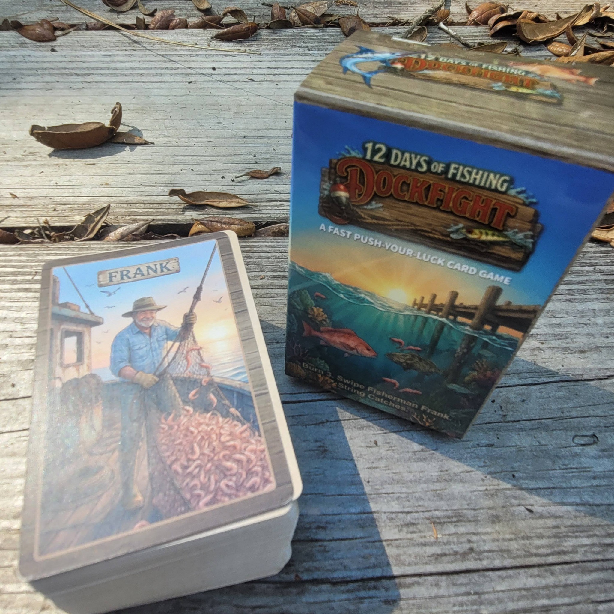 Dock Fight Standard Edition tuck box and Fisherman Frank card photographed on a weathered dock